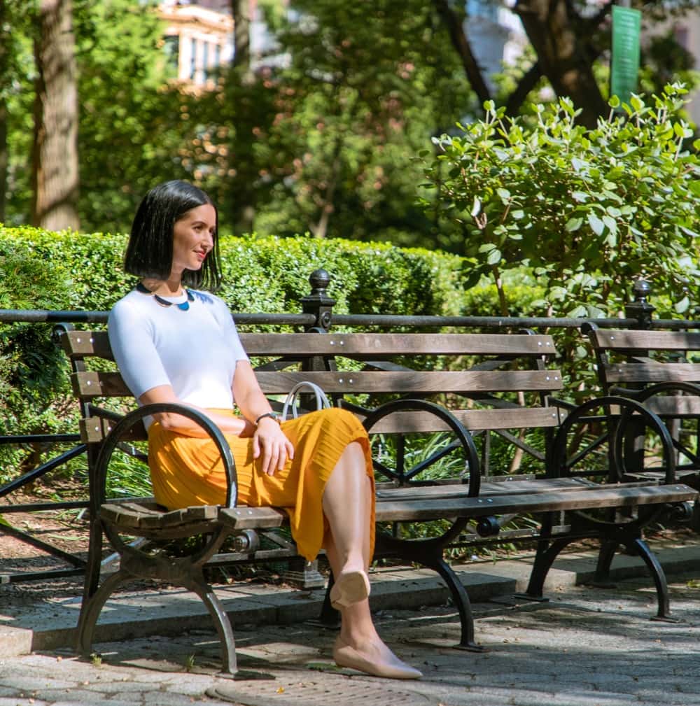 A young Indian woman in a yellow skirt sits on a park bench